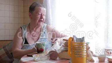 一位老妇人端着一杯热饮和饮料。 他坐在窗边吃早餐。 简单的家居服。